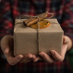 Manos extendiendo un regalo adornado con rodaja de naranja y canela
