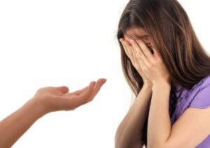 Mano extendida en señal de ayuda a mujer cubriéndose la cara
